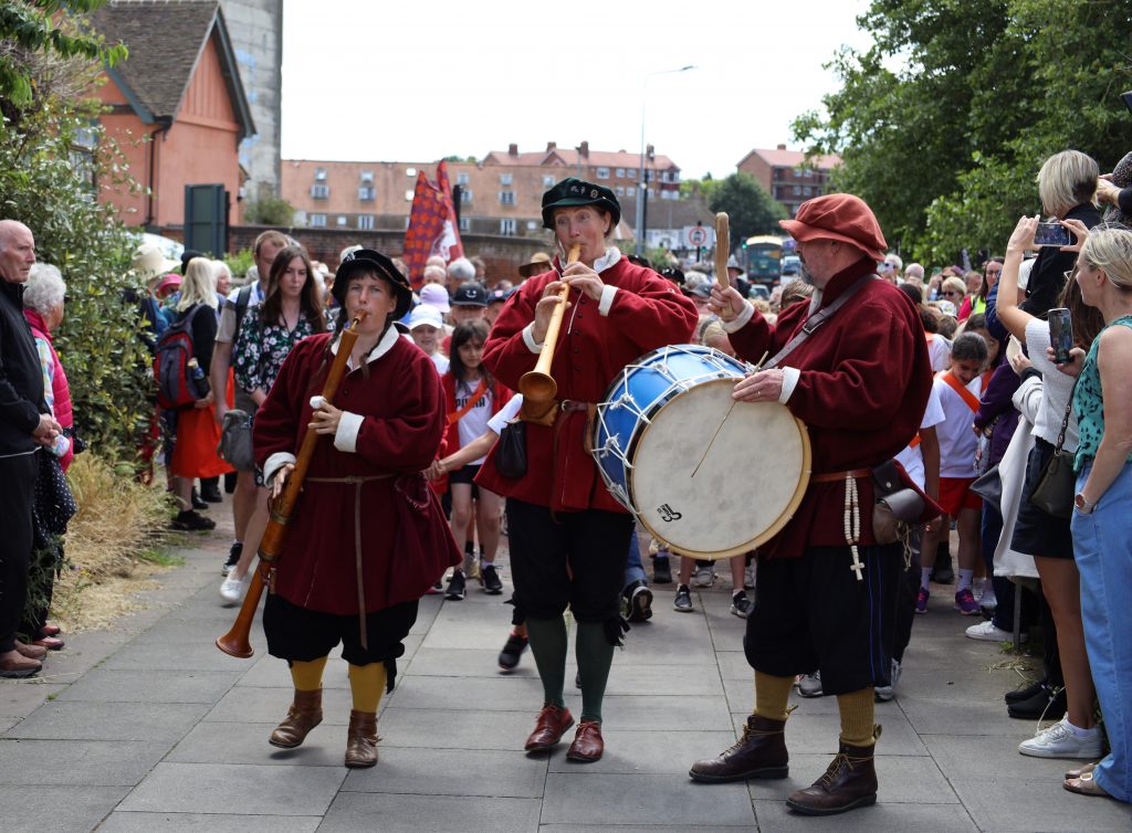 3 musicians in tudor clothing playing period instruments leading a parade of 300 children