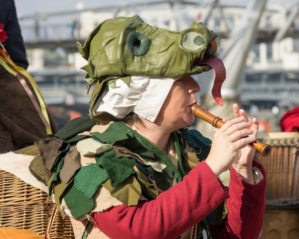 Emma playing the recorder dressed in Tudor period clothing with a dragon mask on her head like a hat