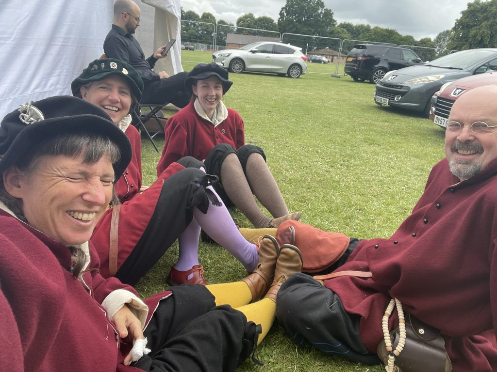 4 musicians in tudor period clothing sat on the grass waiting to play