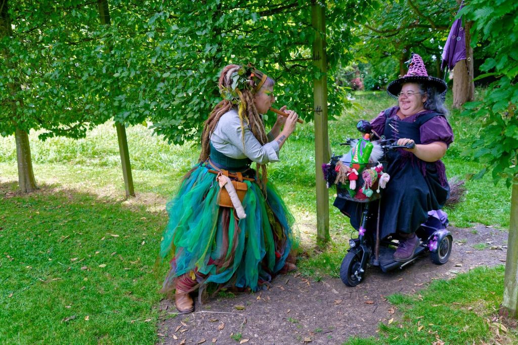Emma dressed as a dryad playing the recorder at a witch on a mobility scooter