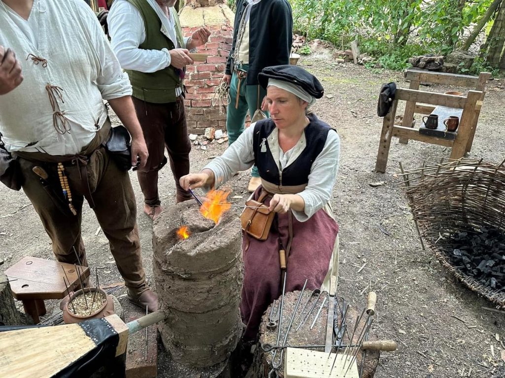 Emma in tudor clothing over a furnace melting glass to make a bead